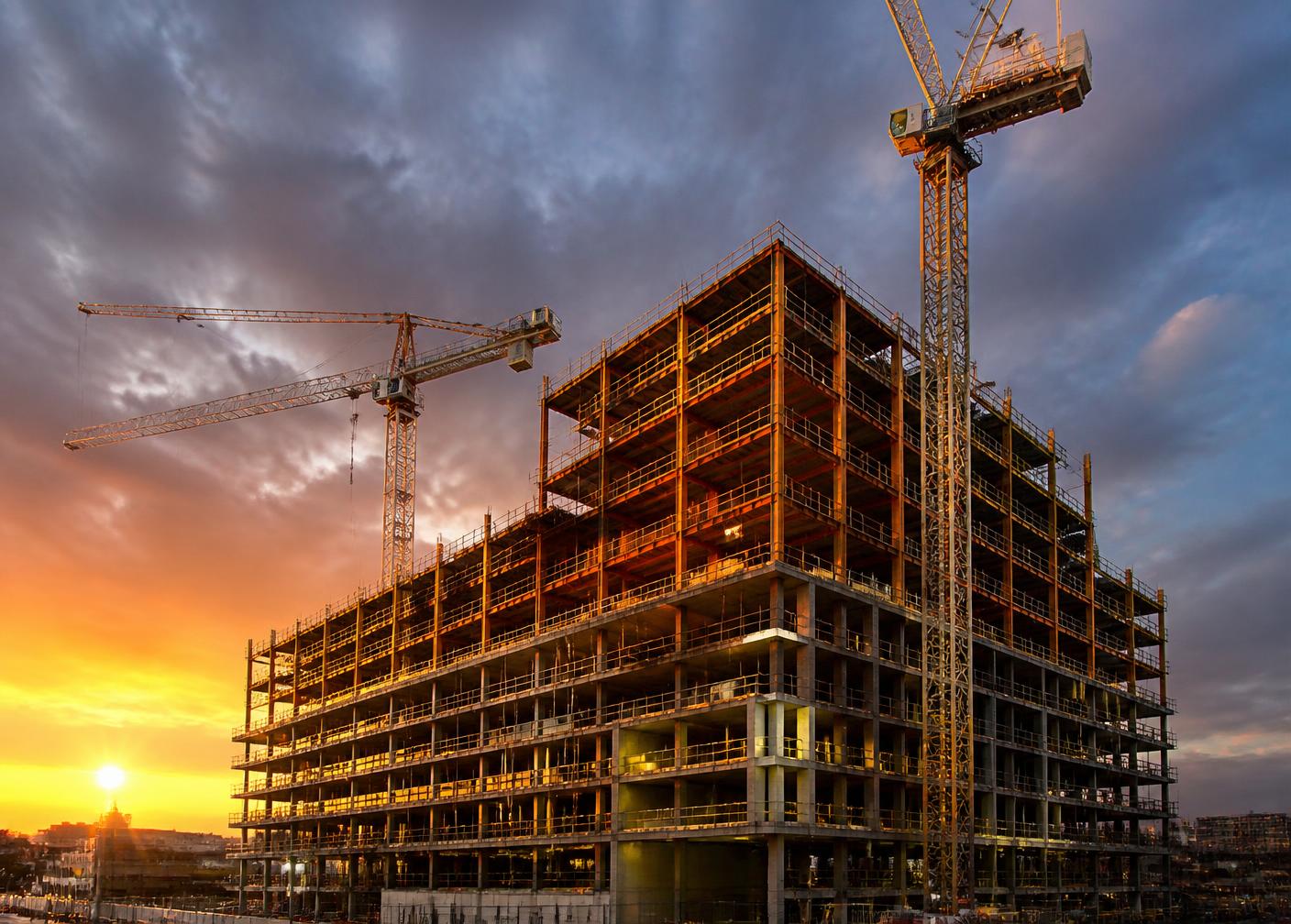 Multi-storey building under construction with tower cranes at sunset